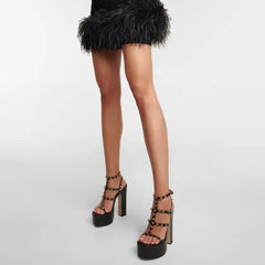Black platform sandals with studded details worn with a black feathered skirt on a white background