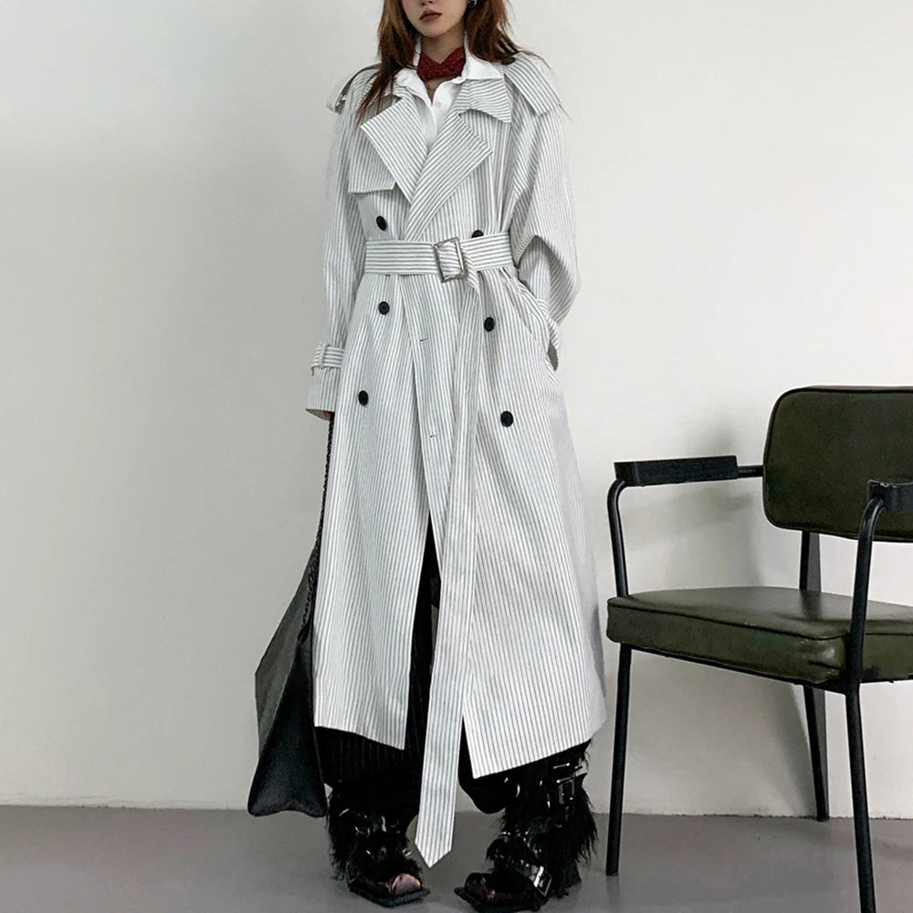 Person wearing a long black and white striped trench coat in a minimalistic setting.