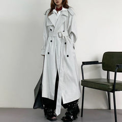 Person wearing a long black and white striped trench coat in a minimalistic setting.