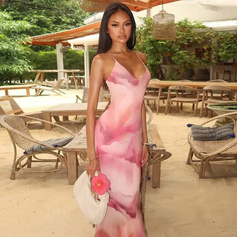 Woman in a pink floral dress standing outdoors with tables and chairs in the background