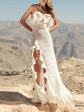 Woman in a white lace dress standing on a rocky landscape with mountains in the background