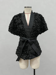 Black floral-patterned top with a belt on a mannequin against a gray background