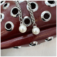 Close-up of a leather product with metal eyelets and pearl charm