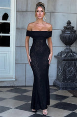 Woman wearing a black off-shoulder lace dress standing in front of a stone wall.