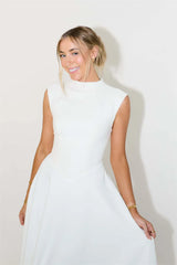 Woman wearing a white sleeveless dress against a plain background