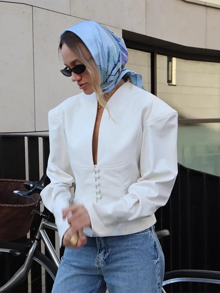 Person wearing a white jacket and blue jeans with a headscarf outdoors.