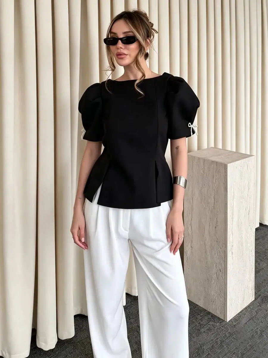 Black puff sleeve peplum blouse with boat neckline and bow detail on sleeve.