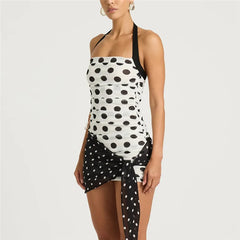 Woman wearing a black and white polka dot halter top with a matching skirt on a light gray background