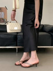 Person wearing black pants and sandals, holding a beige quilted handbag in a minimalistic setting.