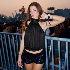 Woman in black top and sequin shorts at a concert with a crowd and stage in the background