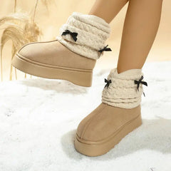 Tan winter boots with white fuzzy tops and black bows on a snowy background