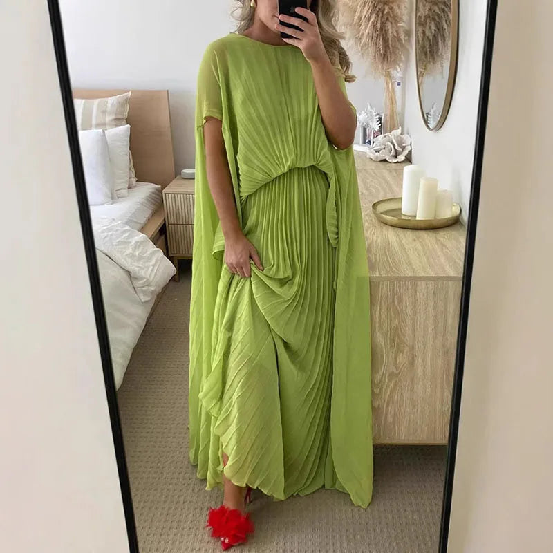 Person wearing a green dress standing in front of a mirror in a bedroom.