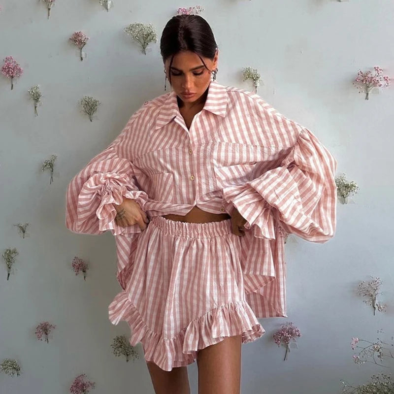 Woman wearing a pink and white checkered outfit against a floral wallpapered wall.