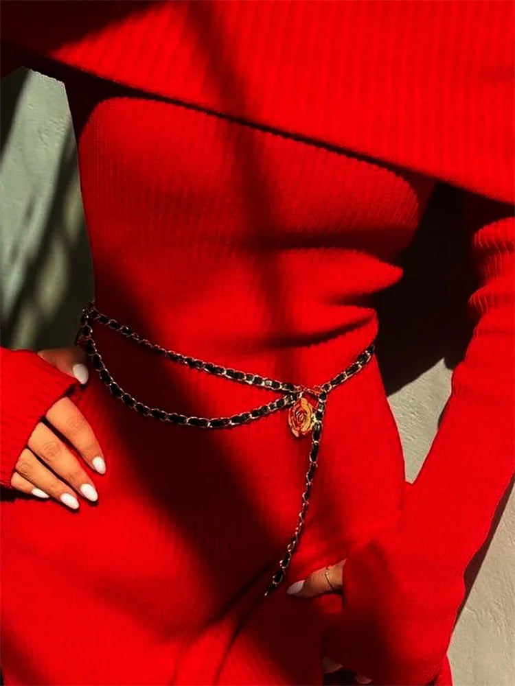 Person wearing a red sweater with a black chain necklace featuring a red gemstone.