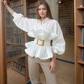 Woman wearing a white blouse with ruffled details and beige pants in a library setting