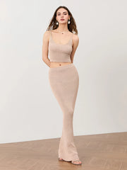 Woman wearing a beige sleeveless top and flared pants on a plain background