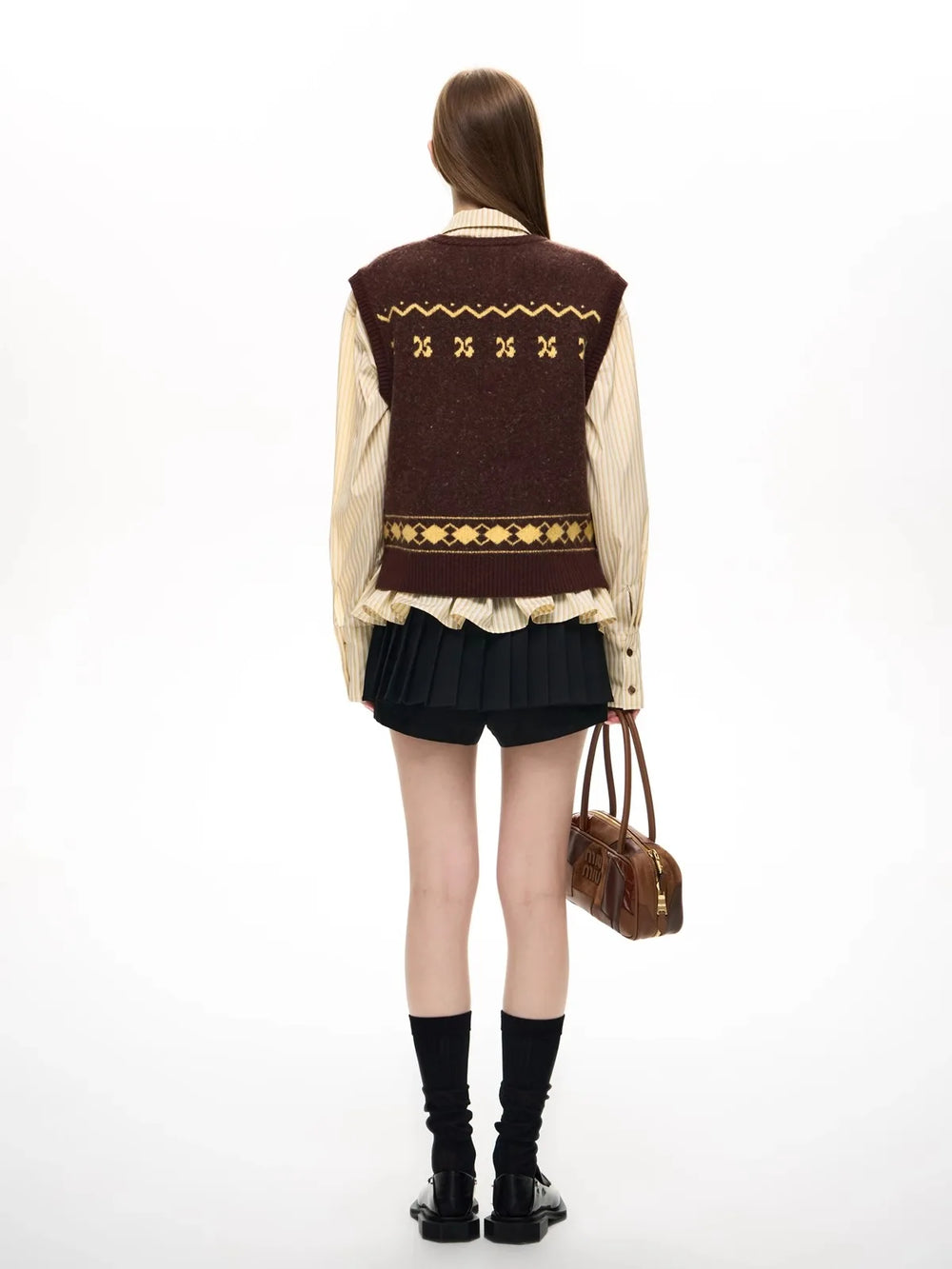 Person wearing a brown patterned vest over a cream shirt with black shorts and boots, holding a brown bag on a white background.