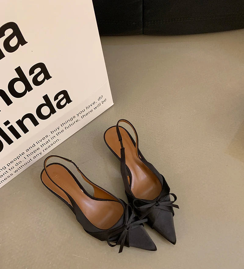 Pair of black slingback shoes with brown soles on a beige surface, next to a white box with text.