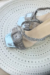 Silver high-heeled shoes with intricate designs on a textured surface
