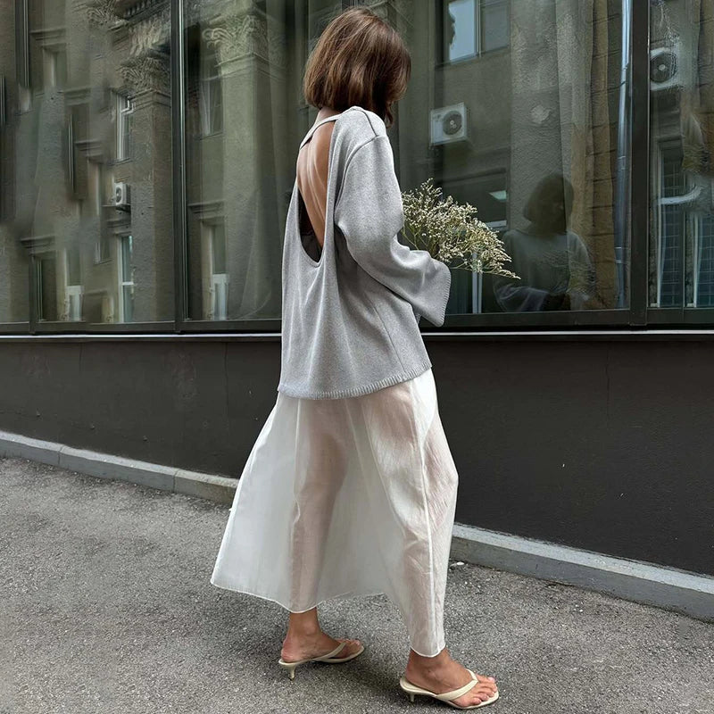 Woman walking on a street wearing a light gray sweater and white pants.