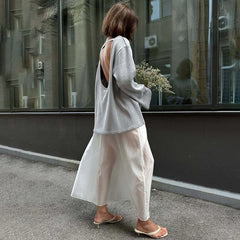 Woman walking on a street wearing a light gray sweater and white pants.