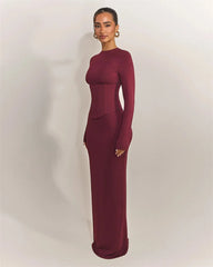 Woman wearing a burgundy long-sleeve gown against a plain background