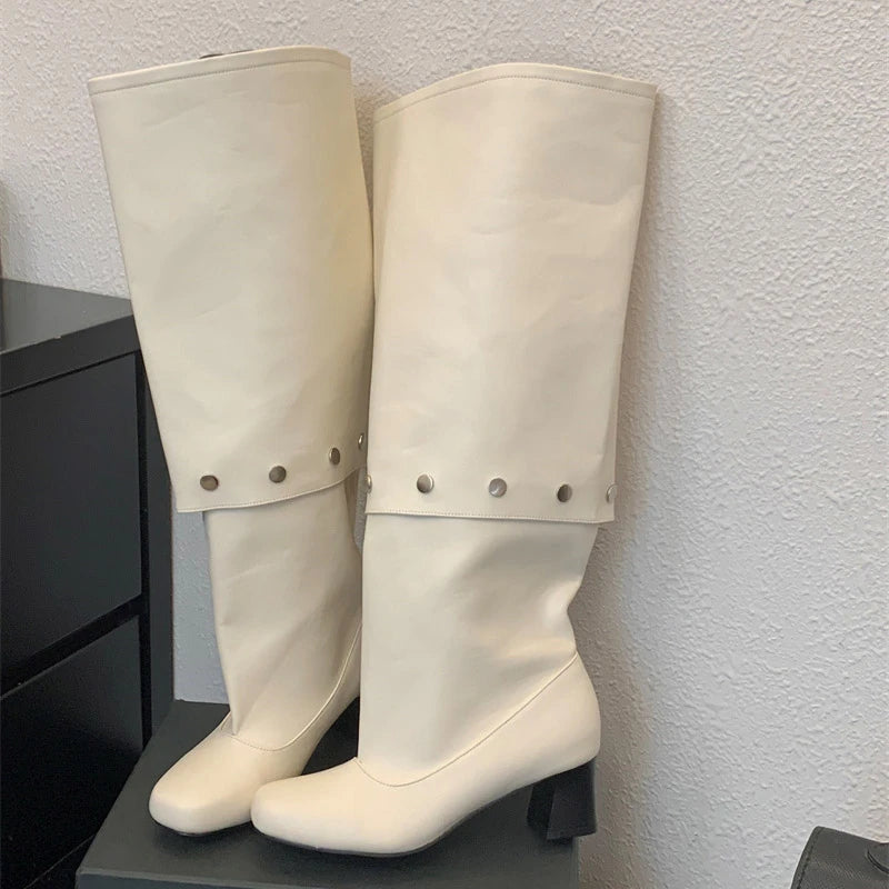 Pair of white knee-high boots with decorative buttons on a black surface against a light gray wall.