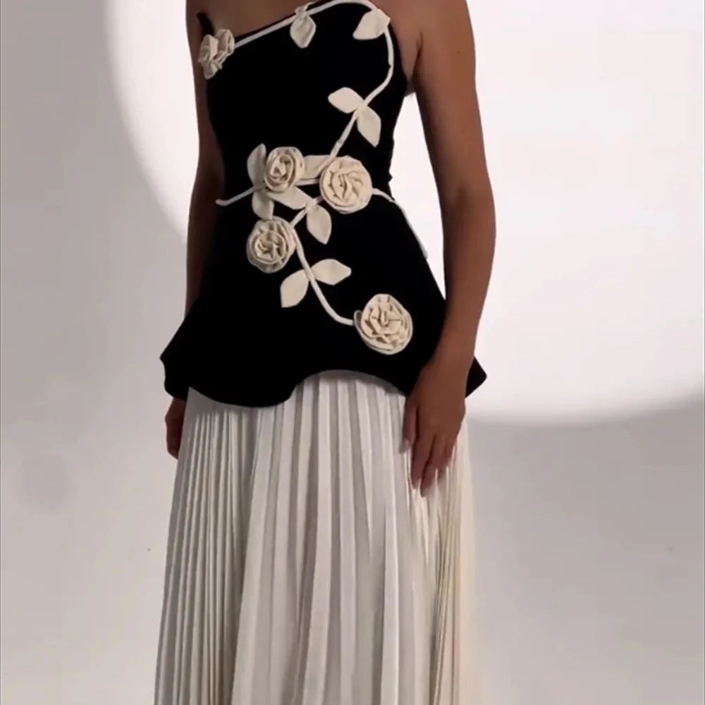 Black top with white floral designs and a white pleated skirt on a neutral background