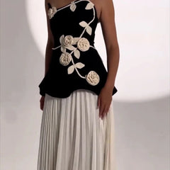 Black top with white floral designs and a white pleated skirt on a neutral background