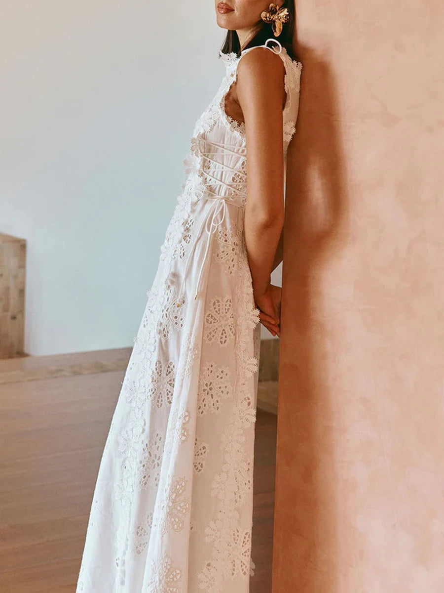 Woman wearing a white lace dress standing against a neutral wall.