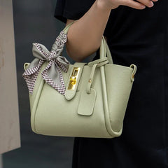 Light green handbag with a bow held by a person against a dark background