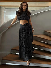Black polka dot sleeveless crop top and flowing maxi skirt on a woman standing on stairs
