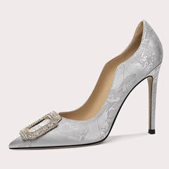 Silver high-heeled shoe with decorative buckle on a light gray background