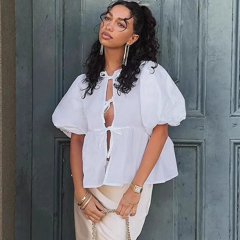 Woman wearing a white blouse with puff sleeves in front of a gray door.