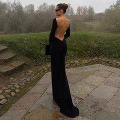 Person wearing a black open-back evening gown standing outdoors on a stone path.