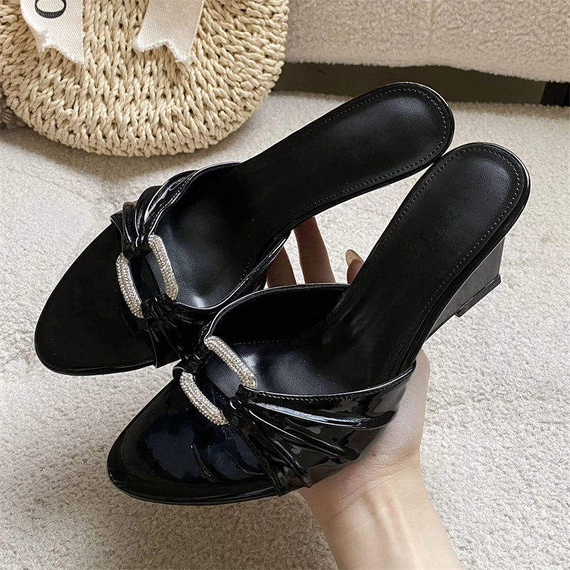 Black patent leather wedge slippers with crystal buckle and pleated detail.