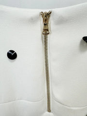 Close-up of a white garment with a gold zipper and black buttons on a light gray background