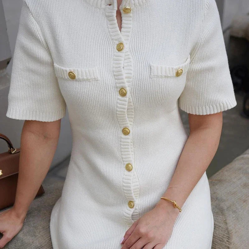 White ribbed dress with gold buttons worn by a person, sitting on a surface.