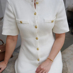 White ribbed dress with gold buttons worn by a person, sitting on a surface.