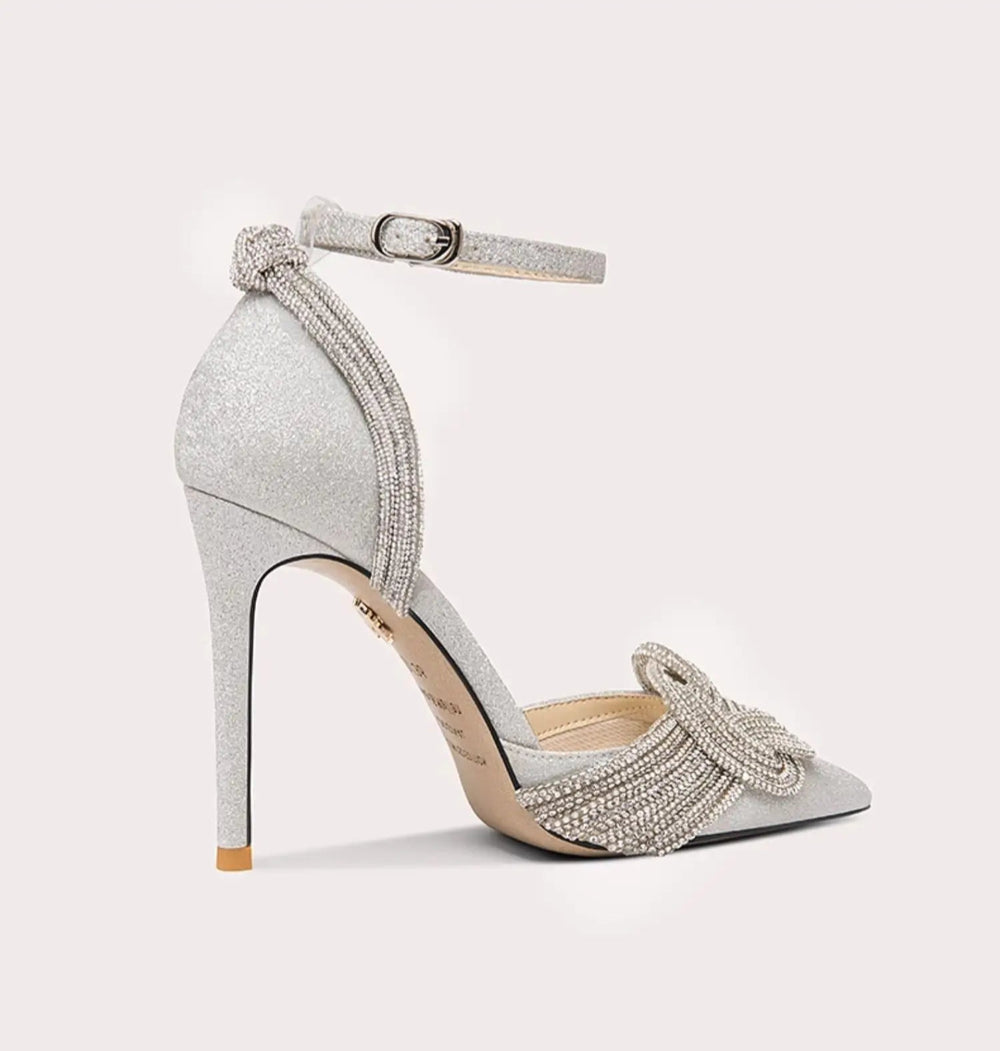 Silver high-heeled shoe with embellishments on a light gray background