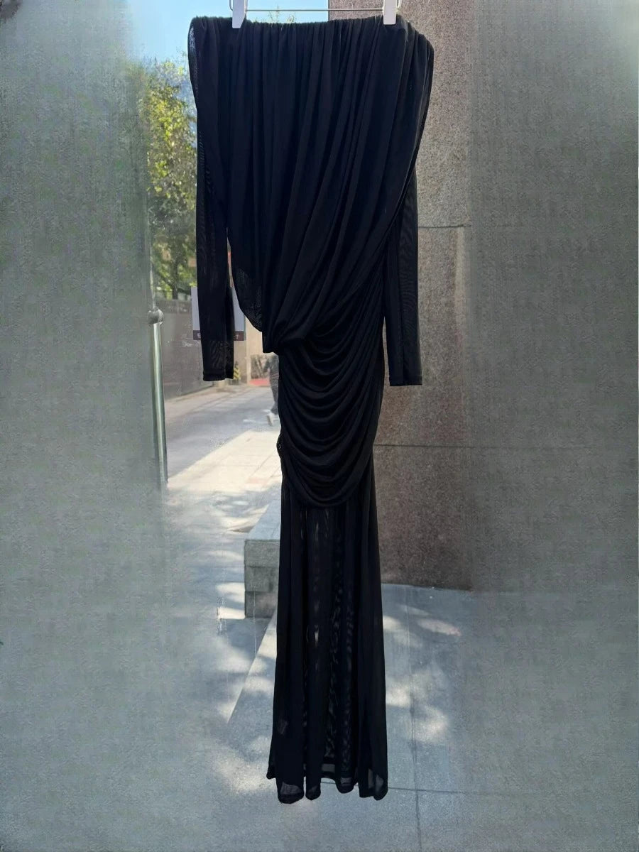 Black evening gown with long train hanging against a neutral wall.