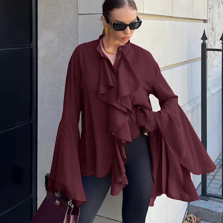 Woman wearing a burgundy ruffled blouse and sunglasses, standing against a building.