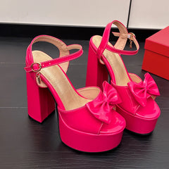 Pink patent leather platform block heel sandals with bow detail.