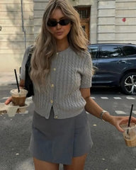 Woman in a light gray cardigan and skirt holding iced drinks on a street.