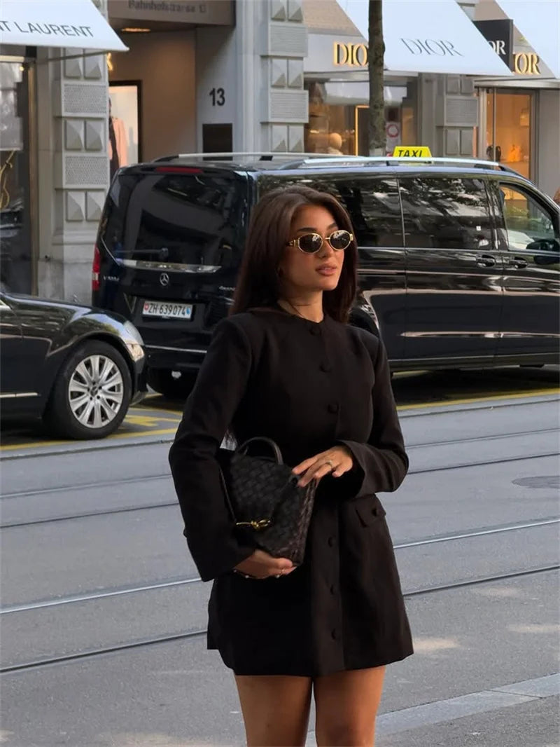 Woman in a black coat standing on a city street with cars and buildings in the background