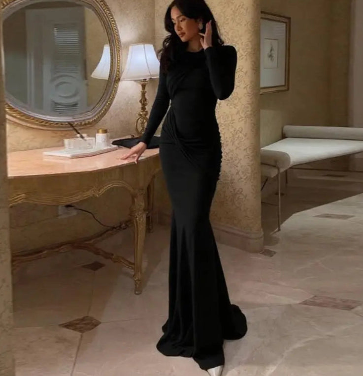 Woman in a black dress standing in a stylish room with a mirror and table.