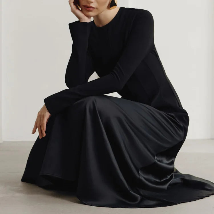 Person wearing a long black dress sitting on a light-colored floor.