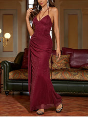 Woman in a burgundy evening gown standing in a room with a couch and lamp.