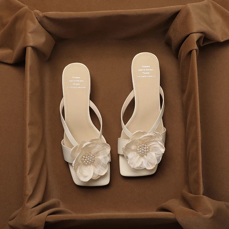 Pair of white sandals with floral decorations on a brown fabric background