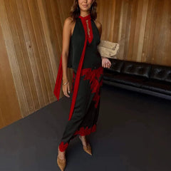 Woman wearing a black dress with red floral details in a room with wooden walls and a black couch.